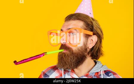 Partyzeit. Feiertage und Feiern. Bärtiger Mann mit Geburtstagskappe und großer Brille mit Noisemaker. Stockfoto