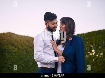 Was ihm gehört, ist von nun an ihr. Eine kurze Aufnahme einer liebevollen jungen Braut, die ihren Bräutigam anlächelt, während sie am Hochzeitstag seine Jacke trägt. Stockfoto