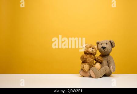 Zwei niedliche braune Teddybären sitzen auf einem gelben Hintergrund, Kinderspielzeug Stockfoto