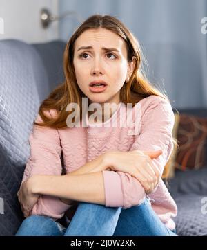 Aufgeregte Frau weinte, während sie auf einem Sofa im Zimmer saß Stockfoto