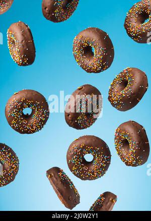 Auf blauem Hintergrund schweben runde Schokoladendonuts mit bunten Zuckerstreuseln Stockfoto