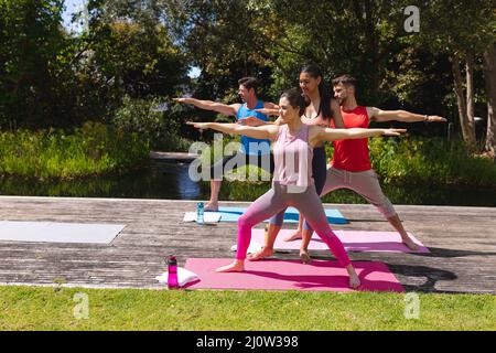 Weibliche Yogalehrerin, die Frauen und Männern beim Training im Park hilft Stockfoto