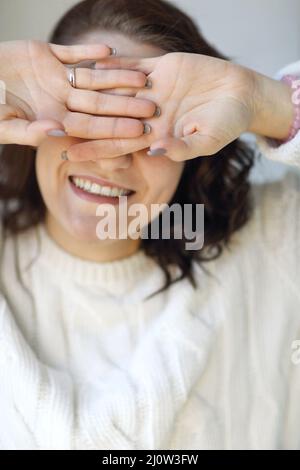 Fröhliche, entzückende Frau in einem Strickpullover, die die Augen mit den Handflächen nach außen schließt und vor der Kamera lächelt Stockfoto