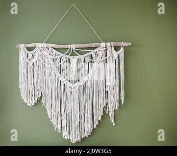 Weiße handgemachte Macrame Dekoration hängt an der grünen Wand, Bohemian Stil dekoratives Element Stockfoto