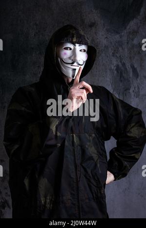 Mittelteil eines Mannes, der die Maske von Anonymous / Guy Fawkes und eine Tarnuniform trägt Stockfoto