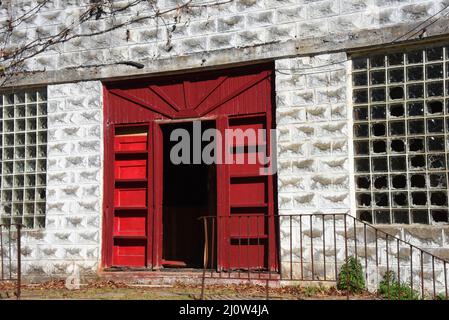 Die Tür des verlassenen Beerdigungshauses in der Geisterstadt Pepper Sauce Alley, Calico Rock, Arkansas, hängt offen. Die Türen sind rot, und viele Glasscheiben machen Stockfoto