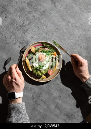 Draufsicht auf einen männlichen Zeiger mit Gabel und Messer zum Essen von Omelett mit Grünpflanzen, Kirschen und Zitronenscheibe Stockfoto