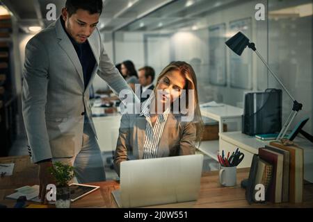 Erfolg funktioniert rund um die Uhr. Aufnahme von Kollegen, die in einer Nachtschicht bei der Arbeit zusammen einen Laptop verwenden. Stockfoto