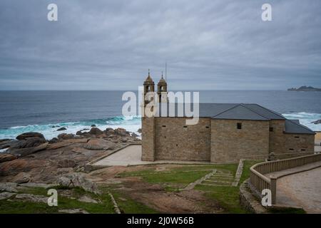Wallfahrtskirche Virxe da Barca in Galicien mit Leuchtturm Cabo Vilan im Hintergrund in Galicien, Spanien Stockfoto