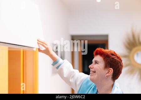 Nahaufnahme einer modernen Frau mit kurzen roten Haaren, nicht binär, die den Kleiderschrank in ihrem Wohnzimmer öffnet. Stockfoto