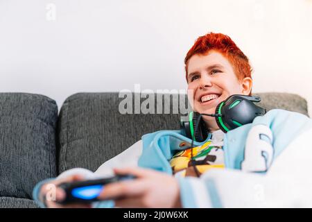 Nahaufnahme einer lächelnden, nicht-binären Person, die Videospiele im Wohnzimmer zu Hause spielt Stockfoto