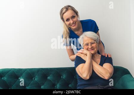 Ältere europäische Frau auf einem Sofa, die die Hand ihrer Betreuerin hält. Beziehung zwischen Patient und Arzt. Hochwertige Fotos Stockfoto