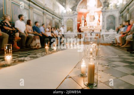 Kerzen in Gläsern brennen während der Hochzeitszeremonie entlang des weißen Teppichs im Tempel Stockfoto