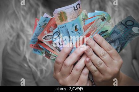 Illustratives Bild von australischem Bargeld, das von einer Person in Schwarz-Weiß im Hintergrund gehalten wird. Notizen und Hände in Farbe. Vermögensgeld Stockfoto