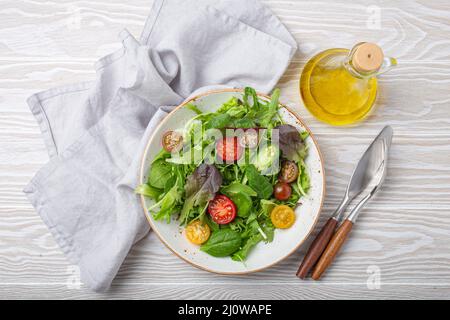 Gemüse gesunder Salat mit roten gelben Kirschtomaten und grünen Salatblättern auf weißer rustikaler Keramikplatte Stockfoto