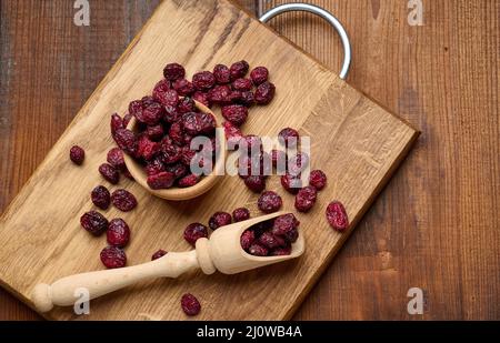 Ein paar getrocknete Preiselbeeren in einem Holzlöffel auf einem braunen Tisch. Köstliche Beeren, Blick von oben Stockfoto