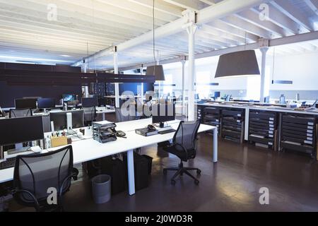 Leere Drehstühle mit Computern an Schreibtischen im beleuchteten modernen Büro Stockfoto