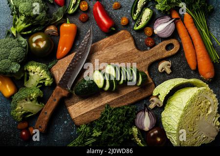 Gehackte Gurke auf Holzschneidebrett mit Messer und gemischtem frischem Gemüse Stockfoto