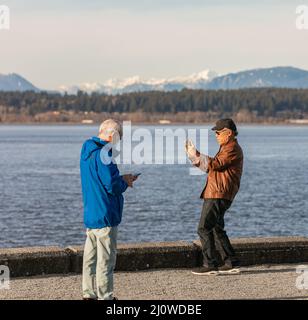 Asiatischer älterer Mann mit einem Smartphone. Ein Mann, der mit seinem Handy im Park Fotos machte. Stockfoto