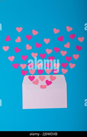 Offener weißer Umschlag mit vereinzelten pfirsichfarbenen Herzformen und pinkfarbenen Herzformen auf blauem Hintergrund Stockfoto