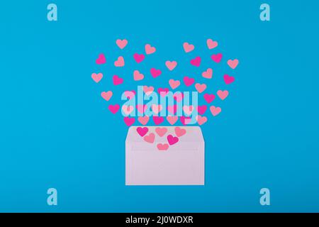 Offener weißer Umschlag mit rosa und pfirsichfarbenen Herzformen auf blauem Hintergrund Stockfoto