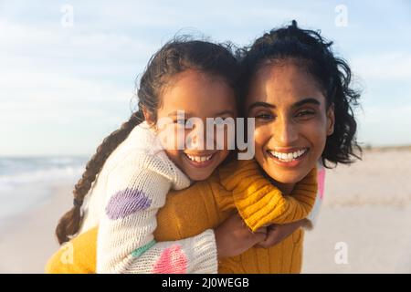 Porträt einer glücklichen Birazialfrau, die bei Sonnenuntergang der Tochter einen Huckepack-Ritt gibt Stockfoto