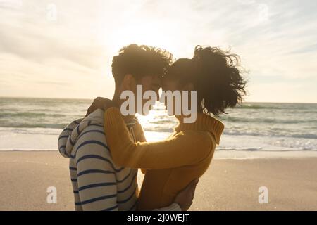 Seitenansicht eines liebenden Biracial Paares, das während des Sonnenuntergangs von Angesicht zu Angesicht am Strand steht Stockfoto