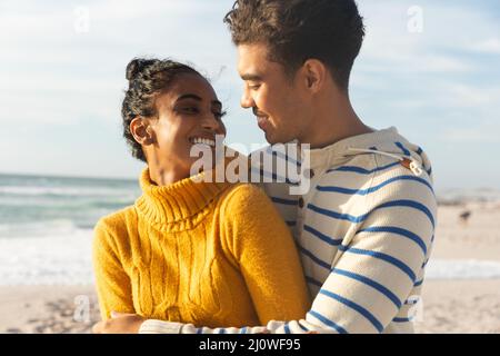 Lächelndes Biracial Paar, das sich anschaut, während es den sonnigen Tag am Strand genießt Stockfoto