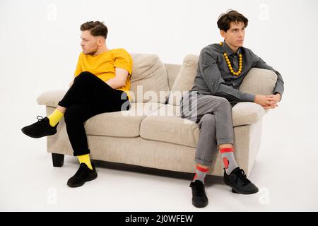 Zwei Freunde streiteten und Sat auf den gegenüberliegenden Seiten des Sofas. Männer sind in einem Streit und sitzen auf der Couch in einem Abstand von jedem O Stockfoto