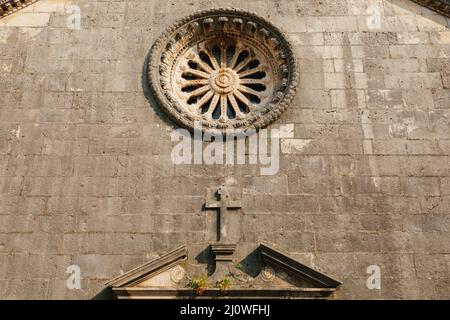 Rosenfenster mit Ornamenten an der dunklen Steinmauer der Kirche über dem Eingang Stockfoto