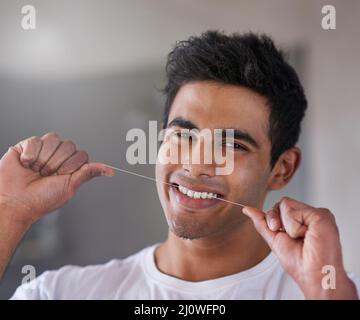 Halten Sie es sauber in den Zwischenräumen. Porträt eines glücklichen jungen Mannes, der zu Hause seine Zähne mit Zahnseide verputzt. Stockfoto