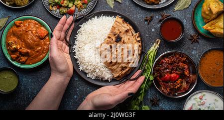 Weibliche Hände servieren ein indisches, ethnisches Buffet auf einem rustikalen Betontisch Stockfoto