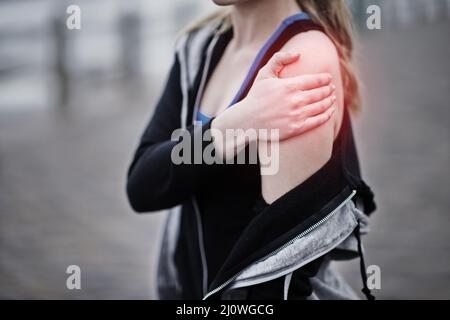 Sie blieb durch eine Verletzung in ihren Spuren stehen. Kurzer Schuss einer jungen Frau, die ihre verletzte Schulter hält. Stockfoto