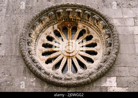 Rosenfenster mit Ornamenten und Mustern an der dunklen Steinwand der Kirche Stockfoto