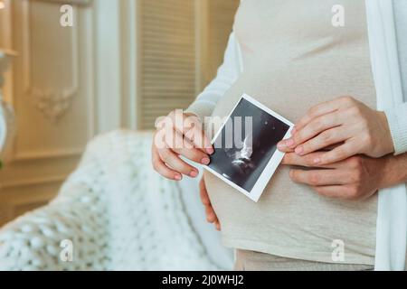 Familienplanung. Kurzer Schuss eines liebenden Mannes, der seine Schwangere umarmt und Ultraschalluntersuchung in den Händen hält, Mann und Frau in Ameise Stockfoto