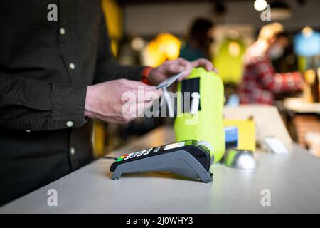 Der Verkäufer hält das Zahlungsterminal, während er den Beleg für den Abschluss des Kaufs hält. Nahaufnahme der Hände. Konzept von NFC, Business und Bank Stockfoto