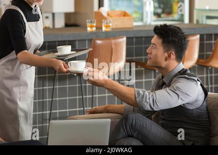 Die junge Kellnerin bietet dem Geschäftsmann eine Tasse Kaffee an Stockfoto