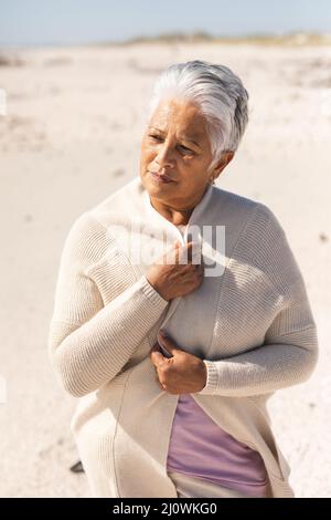 Ältere Birazialfrau mit kurzen weißen Haaren und einem Achselzucken, die an sonnigen Tagen den Strand sieht Stockfoto