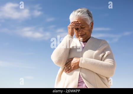 Low-Angle-Ansicht einer angespannten älteren Frau mit der Hand auf der Stirn am Strand gegen den blauen Himmel Stockfoto