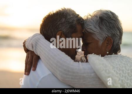 Seitenansicht des liebevollen jungen Biracial Senior Braut und Bräutigam umarmen während des Sonnenuntergangs Stockfoto