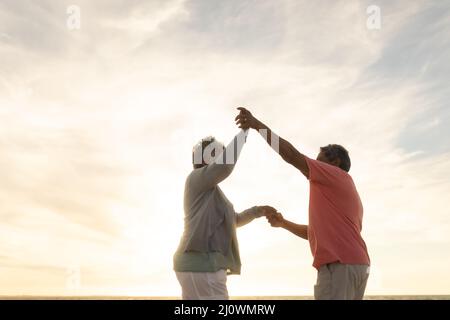 Low-Angle-Seitenansicht Senior multiracial Paar genießen Tanz am Strand gegen Himmel während des Sonnenuntergangs Stockfoto