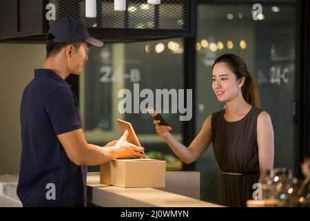 Die chinesische Rezeptionistin zahlt den Lieferer mit ihrem Mobiltelefon Stockfoto