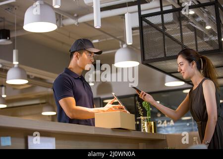 Die chinesische Rezeptionistin zahlt den Lieferer mit ihrem Mobiltelefon Stockfoto