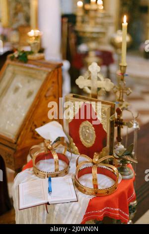 Kreuz, goldene Kronen, Bibel und Kerzenständer stehen auf dem Tisch in der Kirche Stockfoto