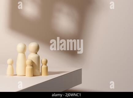 Holzfiguren einer Familie auf einem Schattenhintergrund in Form eines Hauses. Beigefarbener Hintergrund. Heimträume, Hypotheken Stockfoto