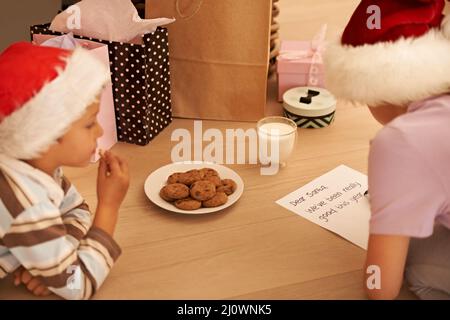 Ich hoffe, dass der Weihnachtsmann die Kekse mögen wird. Ausgeschnittene Aufnahme eines jungen Bruders und einer Schwester, die einen Brief an den Weihnachtsmann schreiben. Stockfoto