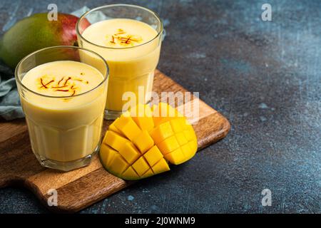 Trinken Sie Mango Lassi in zwei Gläsern auf einem rustikalen Betontisch mit frisch geschnittenem Manfo von oben Stockfoto
