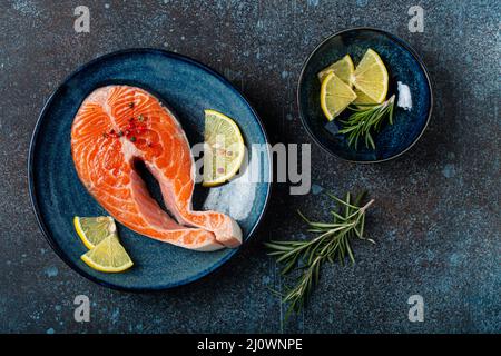 Roher frischer Fisch Lachs Steak von oben auf dem Teller rustikaler dunkler Betonstein Hintergrund Stockfoto