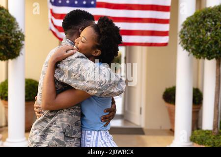 Seitenansicht einer glücklichen afroamerikanischen Frau, die einen Soldaten am Hauseingang umarmt Stockfoto