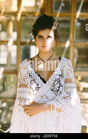 Mädchen in einem weißen Korbkleid steht vor dem Hintergrund eines Holzfensters. Hochformat Stockfoto